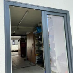 Szare przesuwne drzwi balkonowe z widokiem na zagracony garaż z kamperem w tle.