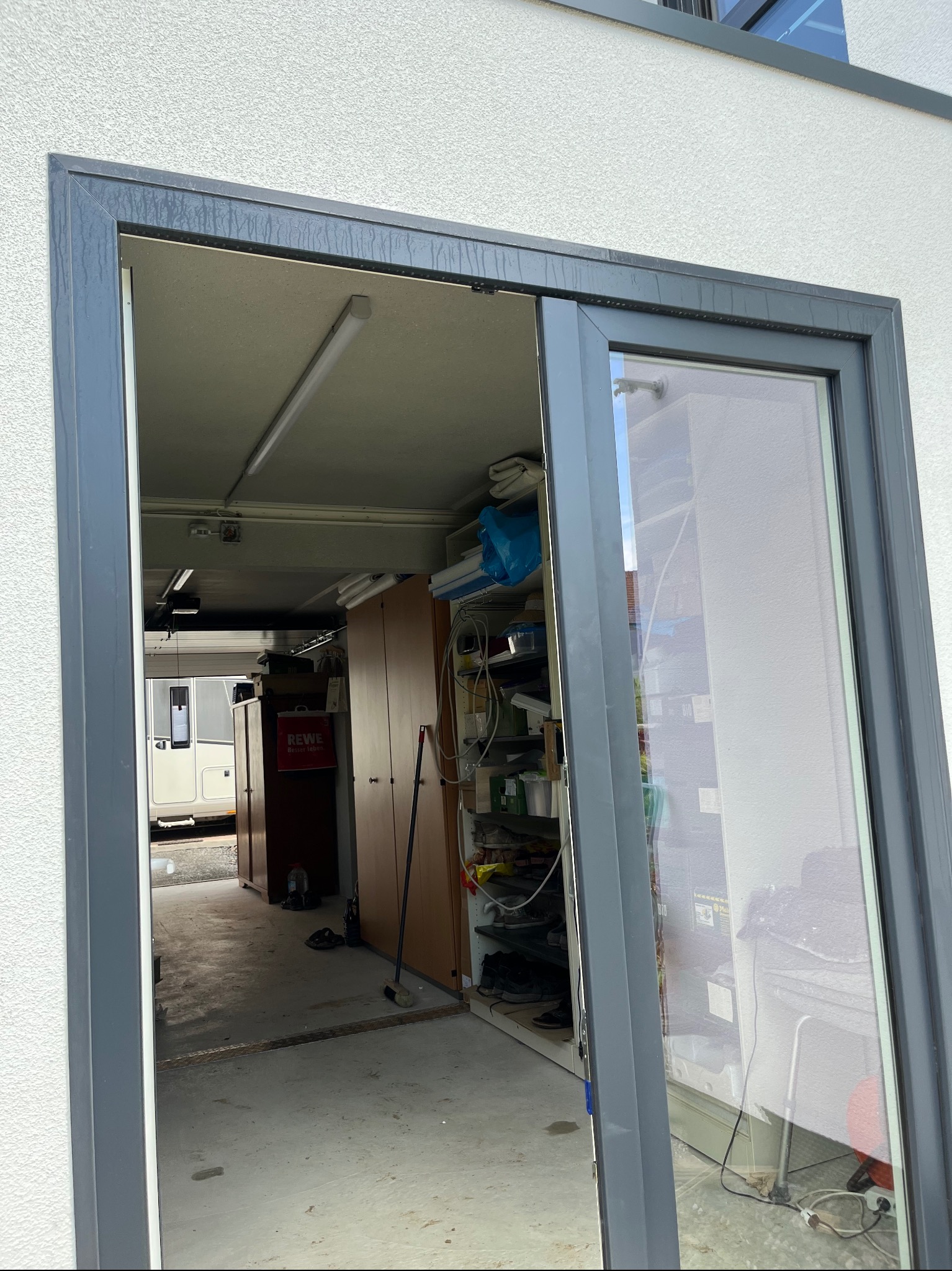 Szare przesuwne drzwi balkonowe z widokiem na zagracony garaż z kamperem w tle.