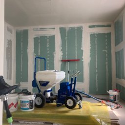 Kamil Błaszczak- Usługi Remontowo-Budowlane - Wnętrze w trakcie prac przygotowawczych do wykończenia ścian, widoczne płyty kartonowo-gipsowe z obrzeżami pokrytymi białą masą, profesjonalny agregat do natrysku masy szpachlowej Texspray, wiadro...