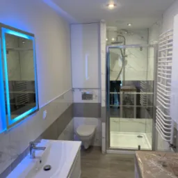 Nowoczesna łazienka z podświetlanym lustrem LED, kabiną prysznicową z chromowanymi detalami i grzejnikiem drabinkowym, wykończona płytkami imitującymi marmur