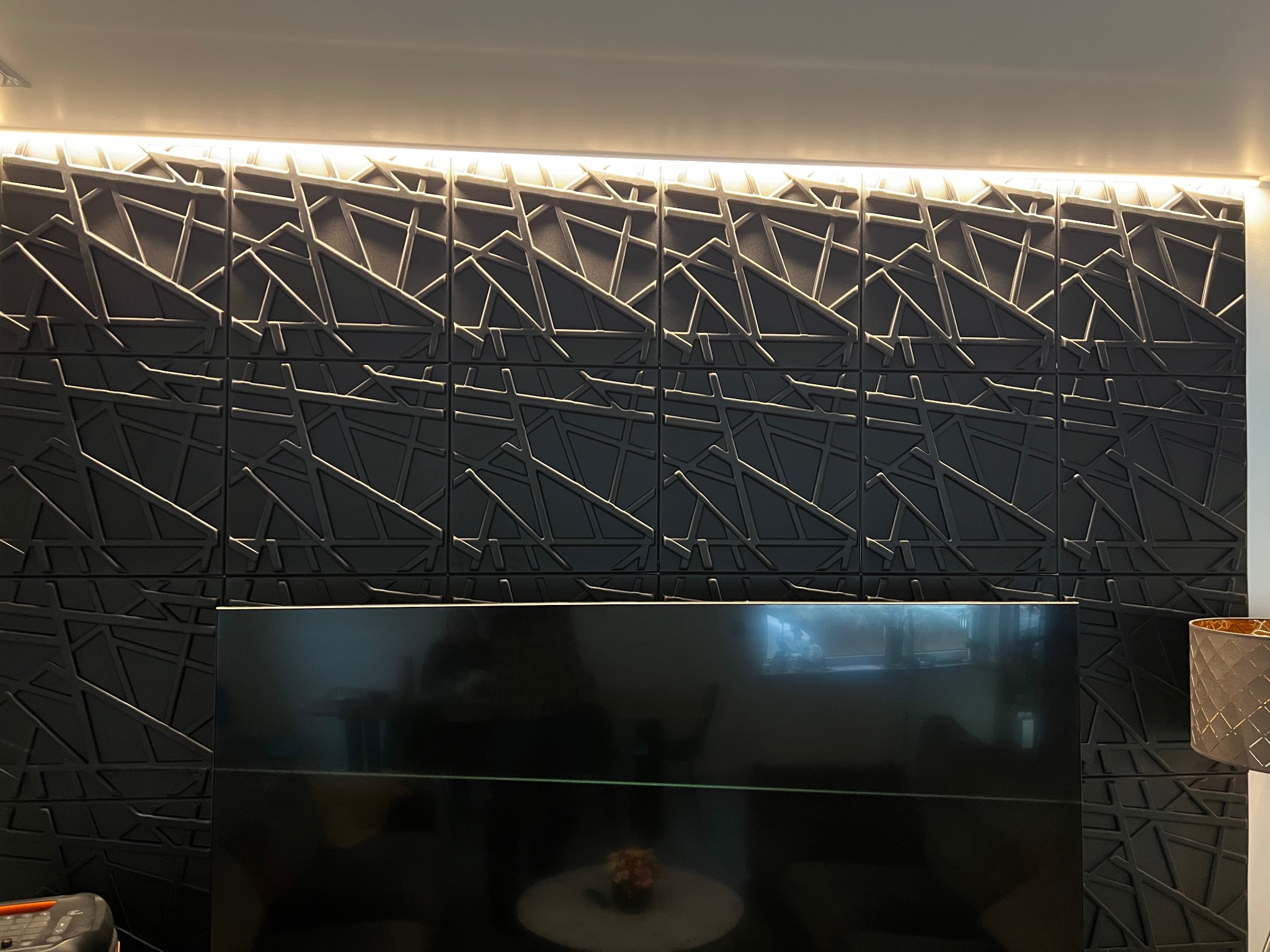 Panel ścienny 3D w kolorze antracytowym z geometrycznym wzorem, podświetlony listwą LED, tworzący nowoczesny efekt dekoracyjny w salonie.