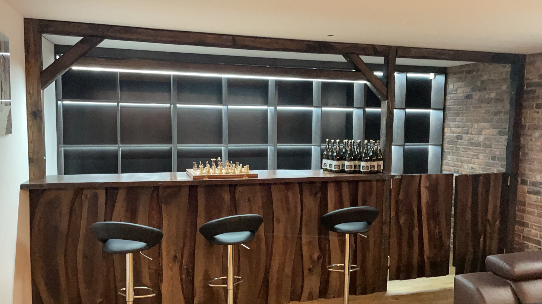 Bar z drewnianym wykończeniem i oświetleniem LED w Barlinku, z szachami i butelkami na blacie, otoczony ceglaną ścianą.