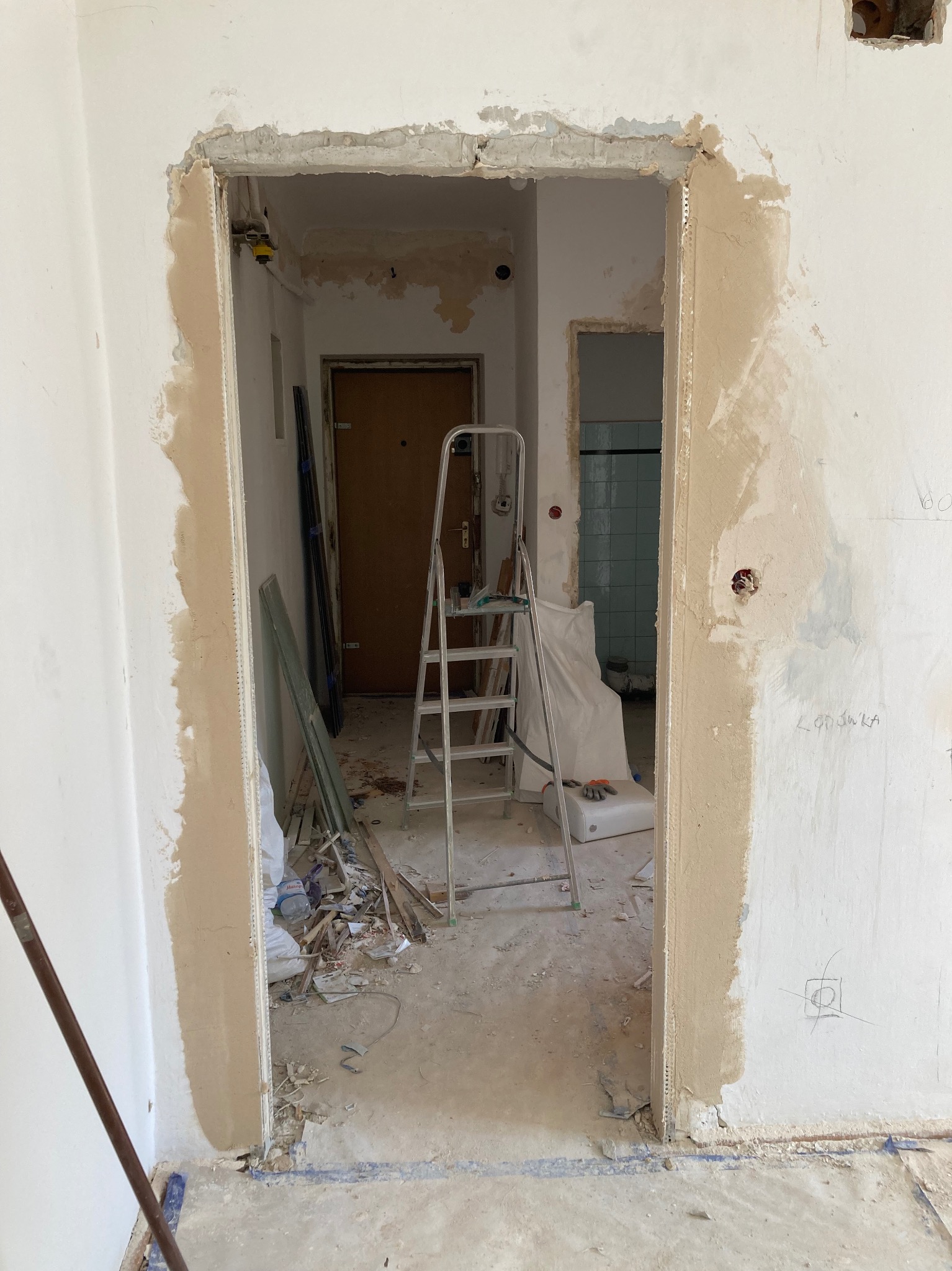 Przygotowanie otworu drzwiowego do osadzenia ościeżnicy, widoczne obrobione krawędzie ścian i surowy stan wykończenia wnętrza z widoczną drabinką i resztkami materiałów budowlanych.
