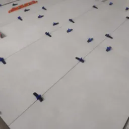 Układanie jasnych, kwadratowych płytek podłogowych z użyciem systemu poziomowania z niebieskimi klipsami i pomarańczową poziomicą w tle.