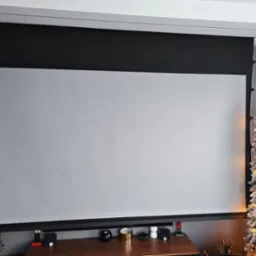 Automatycznie rozwijany ekran projekcyjny w szarej obudowie, zamontowany pod sufitem, z dekoracjami na szafce pod ekranem i choinką z boku, tworzący domowe kino.