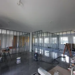 Stelaż z profili metalowych tworzący konstrukcję ścian działowych w surowym stanie, widoczny odkurzacz przemysłowy, narzędzia i drabina, posadzka z wylewki samopoziomującej.