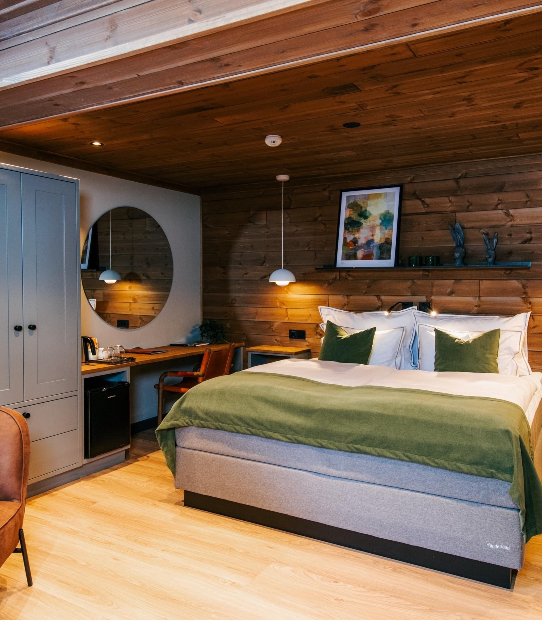 Nowoczesna sypialnia z drewnianą boazerią, okrągłym lustrem i minimalistycznym oświetleniem, utrzymana w stonowanej kolorystyce z akcentami zieleni.