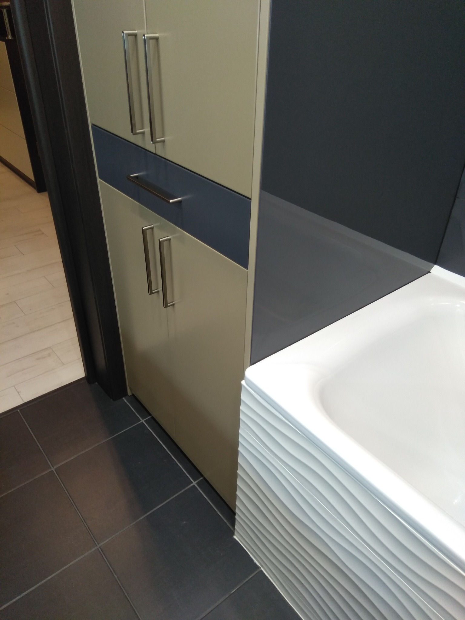 Nowoczesna łazienka: szafka z szufladami w odcieniach beżu i granatu, umywalka z falistym wzorem i ciemna, kwadratowa podłoga z płytek. Minimalistyczny design.