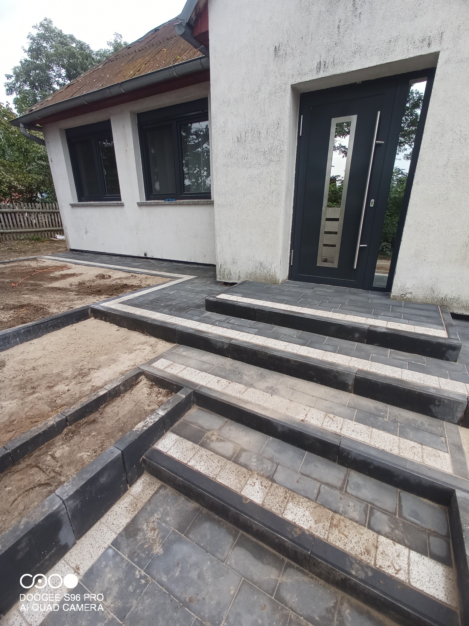 Nowoczesne schody wejściowe i obrzeża z kostki brukowej w trakcie układania, widoczny fragment terenu przygotowany pod dalsze prace brukarskie.