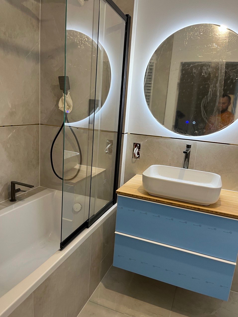 Nowoczesna łazienka z wanną i szklanym parawanem, umywalką nablatową na szafce z bambusowym blatem i okrągłym lustrem z podświetleniem LED, folia ochronna na lustrze.