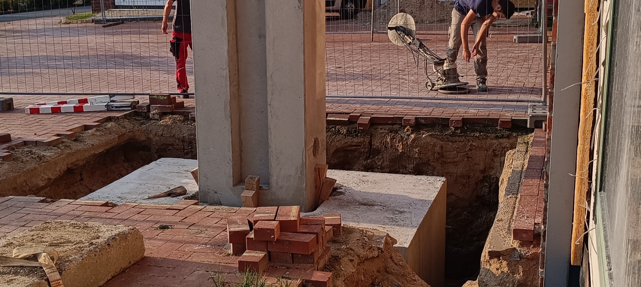 Przygotowanie fundamentów pod budynek z wykopem i elementami betonowymi, widoczne cegły i pracownik zacierający posadzkę