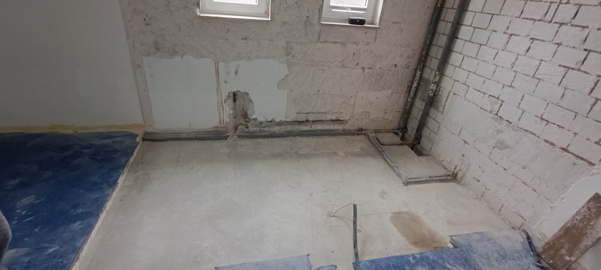 Wnętrze pomieszczenia po usunięciu fragmentu ściany, z widocznymi instalacjami i fragmentami cegieł, zabezpieczone podłogą folią.