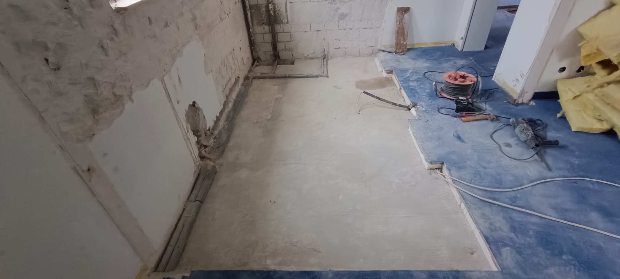Fragment pomieszczenia po skuciu tynku ze ścian i częściowo z podłogi, widoczne narzędzia budowlane: szlifierka kątowa, przedłużacz, dłuto