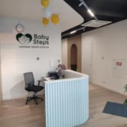 Jasne wnętrze recepcji centrum terapii z biurkiem o falistej strukturze, logo 'Baby Steps' na ścianie i dekoracyjnymi balonami.