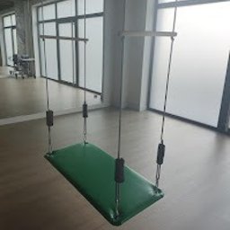 Centrum Terapii Dziecka BABY STEPS Częstochowa - fizjoterapia - logopeda dziecięcy - psycholog dziecięcy - Zielone podwieszane urządzenie rehabilitacyjne z czarnymi uchwytami w jasnym pomieszczeniu z lustrami i drewnianą podłogą.