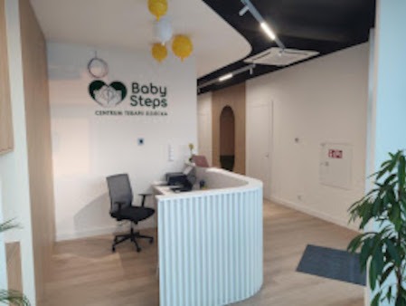 Jasne wnętrze recepcji centrum terapii z biurkiem o falistej strukturze, logo 'Baby Steps' na ścianie i dekoracyjnymi balonami.