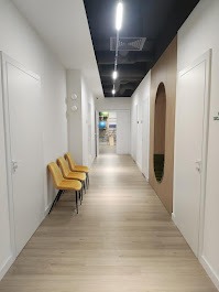 Jasny, nowoczesny korytarz w placówce medycznej z rzędem trzech żółtych krzeseł pod ścianą. Na suficie widoczne podłużne lampy. Po prawej stronie ściana z owalnym, dekoracyjnym wcięciem.