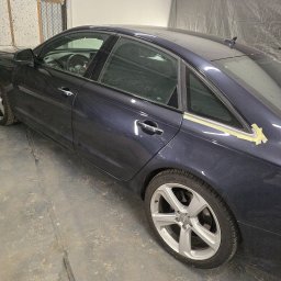 DarkRideGarage - Granatowy samochód Audi A6 w trakcie oklejania, zabezpieczony taśmą malarską na tylnej szybie, widoczny w warsztacie.