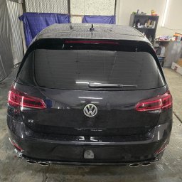 DarkRideGarage - Czarne auto marki Volkswagen Golf R, widziane od tyłu, z przyciemnionymi szybami, pokryte kroplami wody, stoi w garażu.