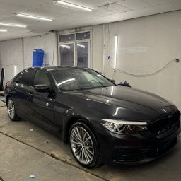 DarkRideGarage - Ciemny sedan BMW po przyciemnianiu szyb, widoczne ciemne szyby boczne i tylna, zaparkowany w warsztacie z betonową podłogą i oświetleniem jarzeniowym.