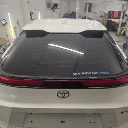 DarkRideGarage - Tylna szyba białego samochodu z napisem 'STOP SMOG GO HYBRID' po procesie zmiany barwy, widoczne drobne zanieczyszczenia na powierzchni.