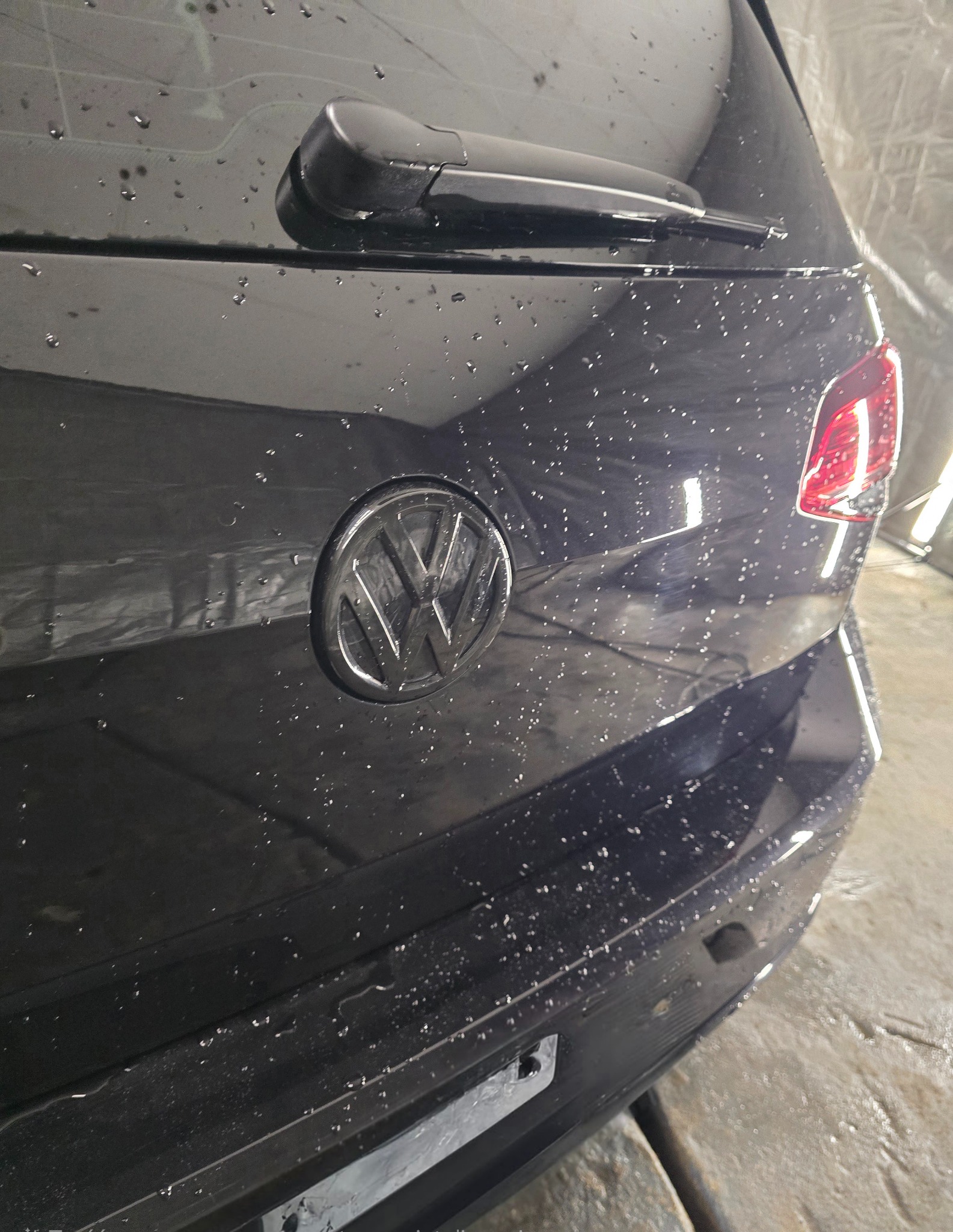 Czarny samochód marki Volkswagen, tylna klapa pokryta kroplami wody, widoczne logo i wycieraczka, po umyciu.