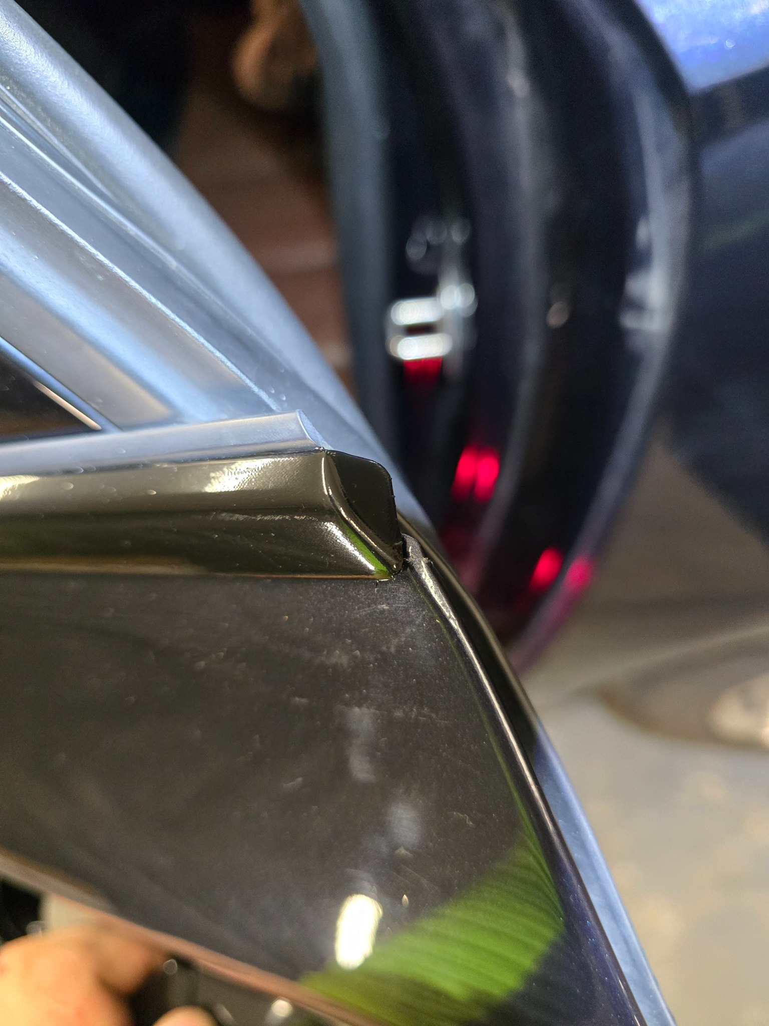 Szczegółowe ujęcie krawędzi karoserii samochodu z nałożoną folią ochronną, widoczne drobne niedoskonałości w spasowaniu na rogu.