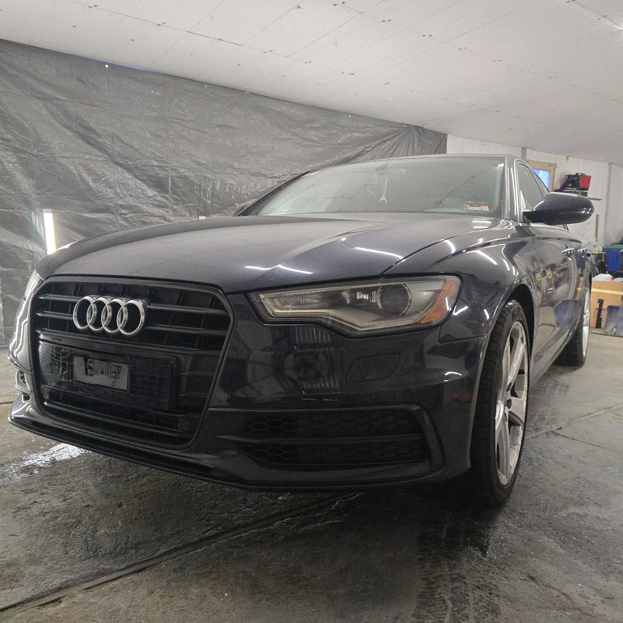 Granatowy samochód Audi A6, widok z przodu, zaparkowany w garażu z szarą plandeką w tle.