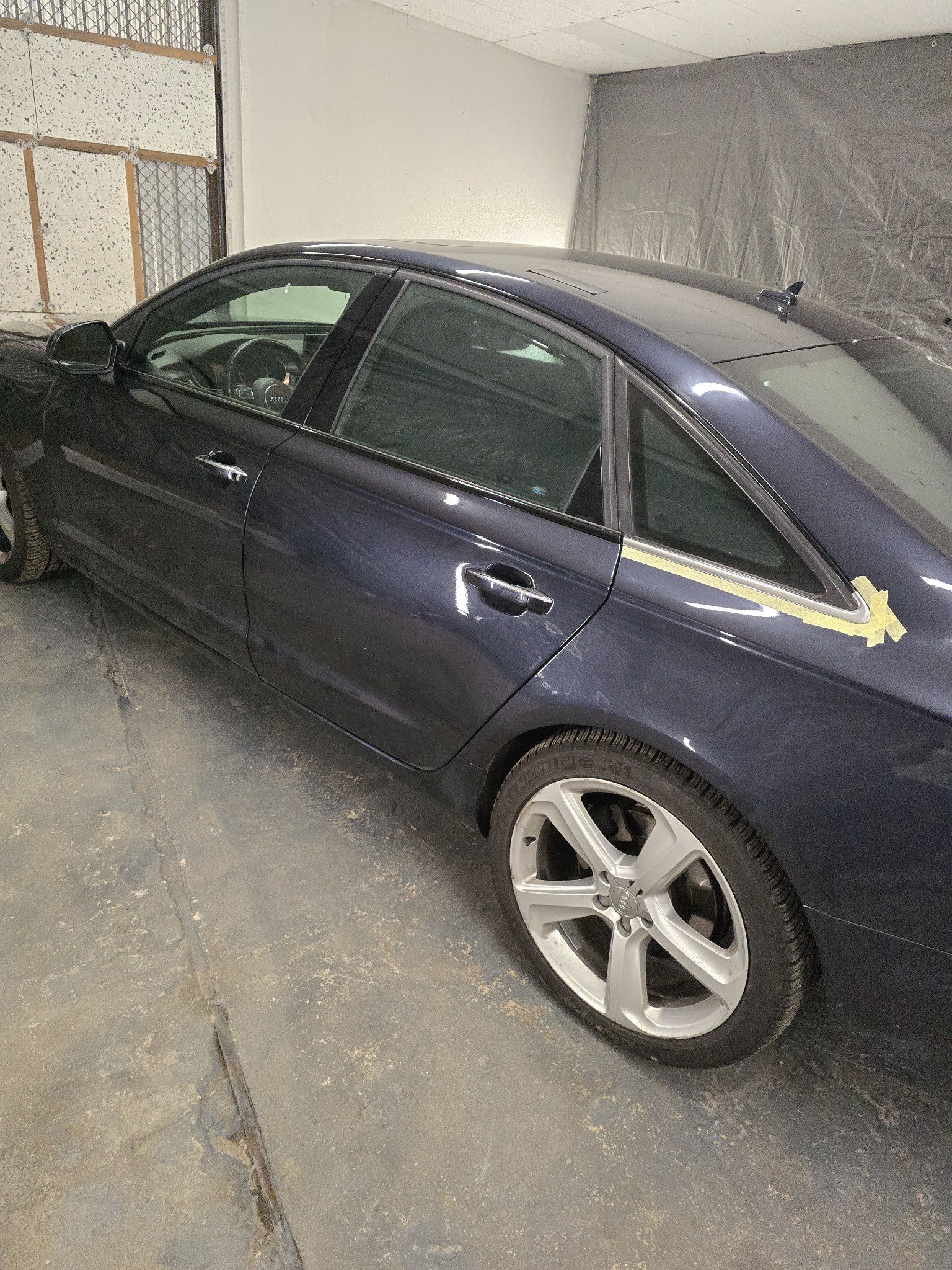 Granatowy samochód Audi A6 w trakcie oklejania, zabezpieczony taśmą malarską na tylnej szybie, widoczny w warsztacie.
