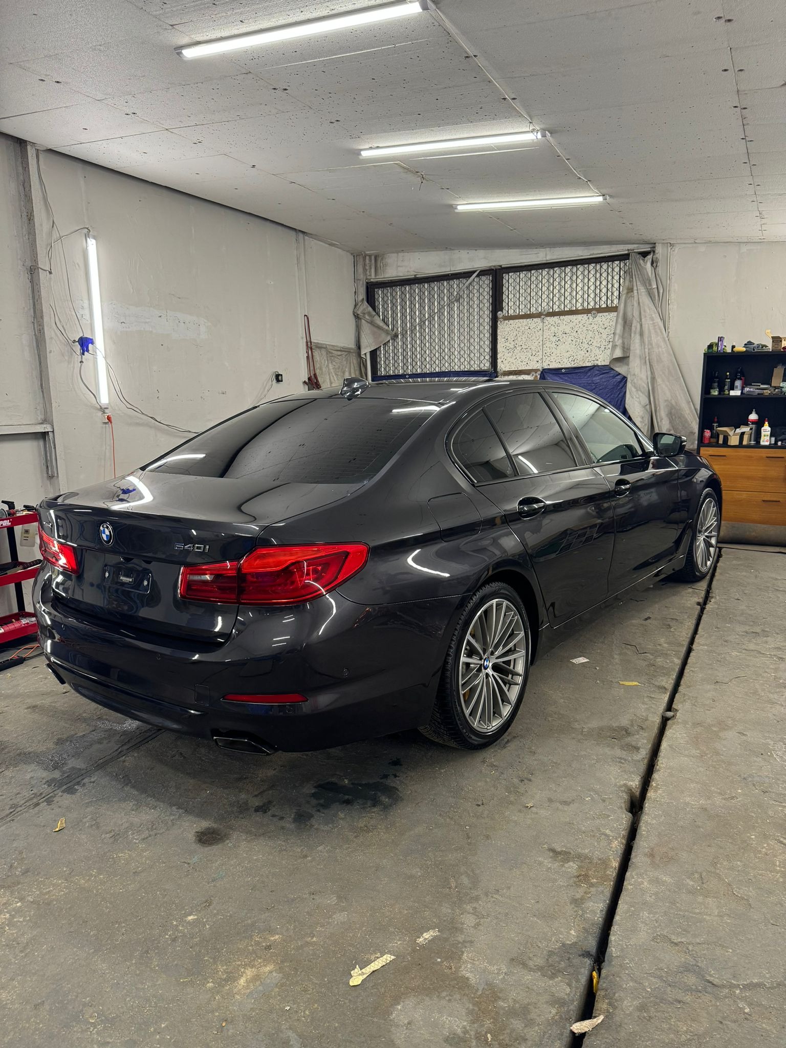 Błyszczący, czarny samochód BMW 540i po myciu, widoczny z tyłu pod kątem w garażu z betonową podłogą i widocznym odpływem liniowym.