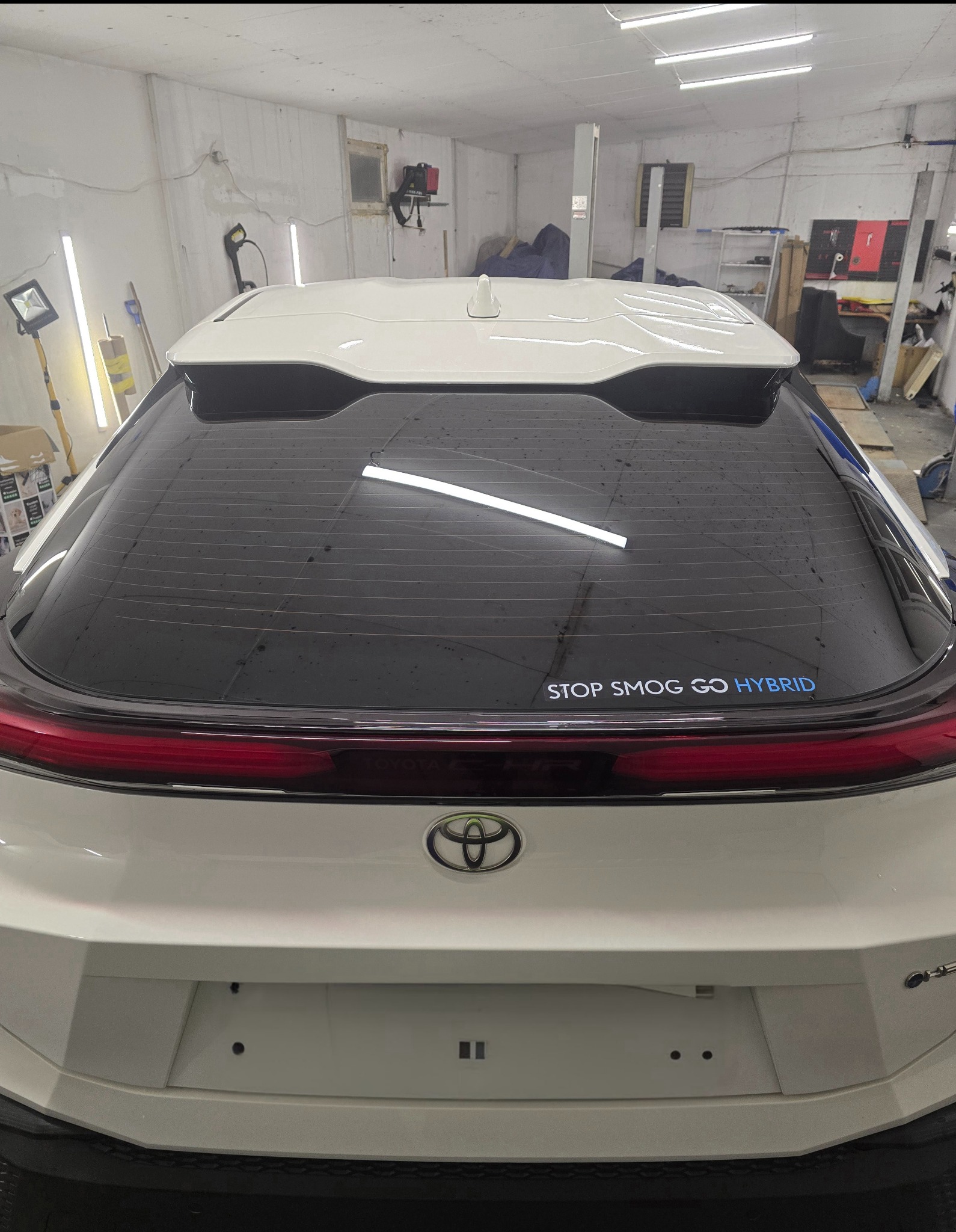 Tylna szyba białego samochodu z napisem 'STOP SMOG GO HYBRID' po procesie zmiany barwy, widoczne drobne zanieczyszczenia na powierzchni.