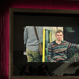 SMART EV - Kino domowe z dużym ekranem wyświetlającym film, podświetlenie LED w kolorze fuksji oświetla ścianę z pionowymi panelami, widoczny sprzęt audio i konsola Playstation 5.