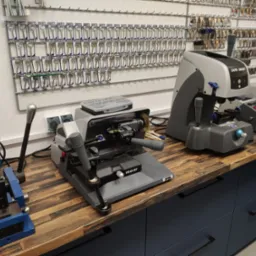 Warsztat z maszynami do kopiowania kluczy Capri Smart i Volga Bit, widok na ścianę z zawieszkami na klucze z opisami.