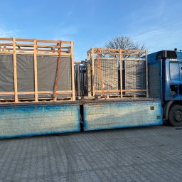 Gold Fence - Ciężarówka z platformą transportuje w drewnianych skrzyniach zabezpieczone panele ogrodzeniowe, widoczne pasy mocujące.