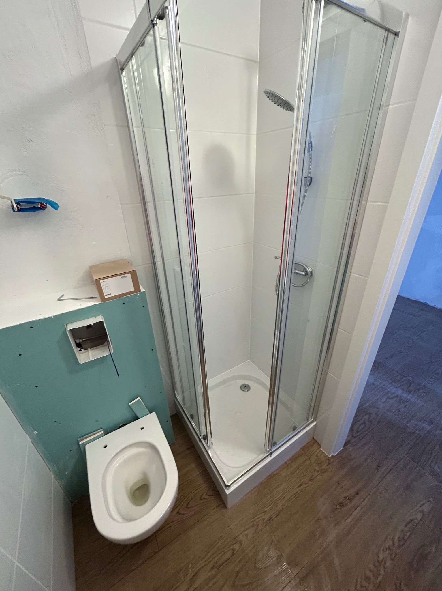 Montaż kabiny prysznicowej i toalety w trakcie prac wykończeniowych łazienki. Widoczne płytki, drewnopodobna podłoga i elementy instalacji.