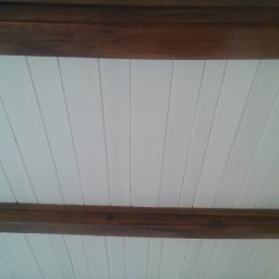 360 GLOBAL INVEST SPÓŁKA Z OGRANICZONĄ ODPOWIEDZIALNOŚCIĄ - Biały sufit z drewnianymi belkami, widoczne ślady remontu na ścianie w tle.