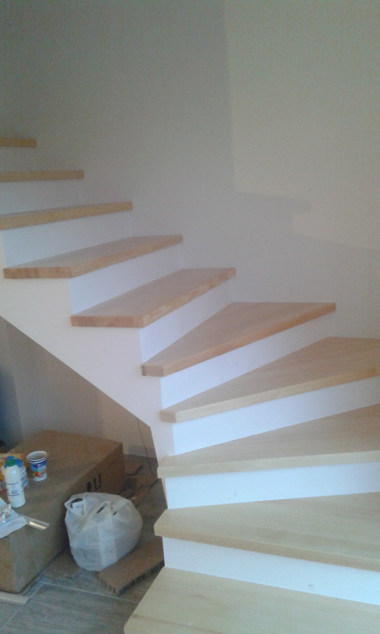 Drewniane schody o jasnych stopniach i białych podstopnicach w trakcie montażu; widoczne materiały budowlane obok.