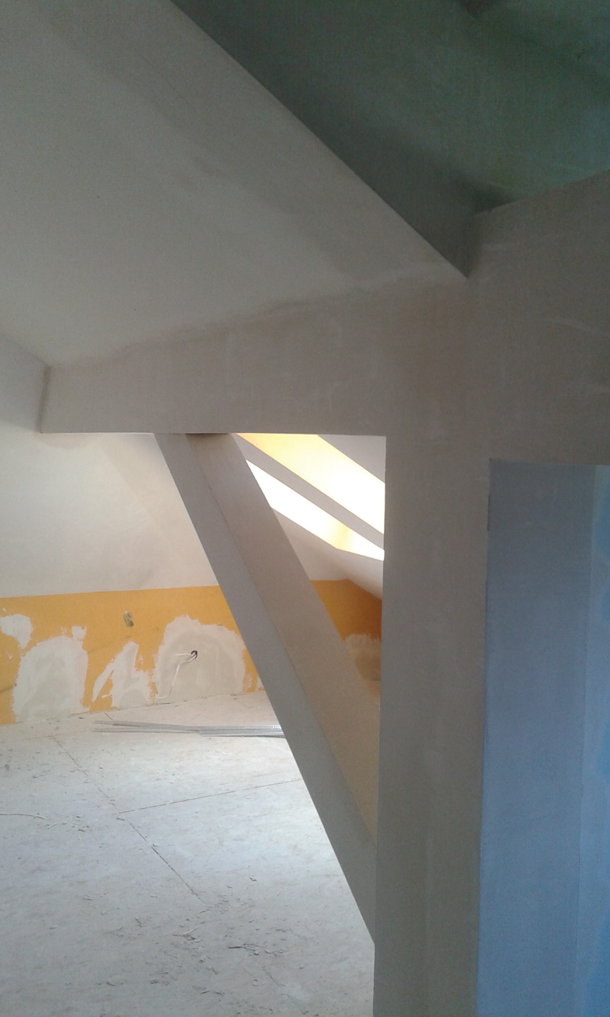 Poddasze w trakcie wykańczania: gładzie na ścianach, konstrukcja pod skosem dachu i listwy przypodłogowe na podłodze.