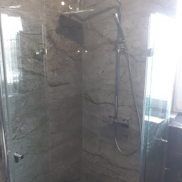 Uslugi budowlane - Szklana kabina prysznicowa z deszczownicą i marmurowymi płytkami ściennymi w odcieniach szarości.