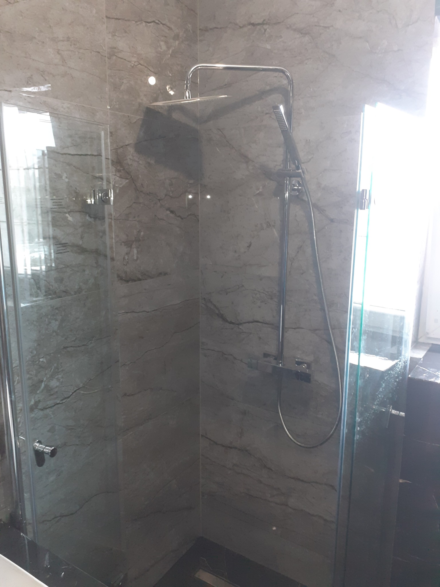 Szklana kabina prysznicowa z deszczownicą i marmurowymi płytkami ściennymi w odcieniach szarości.