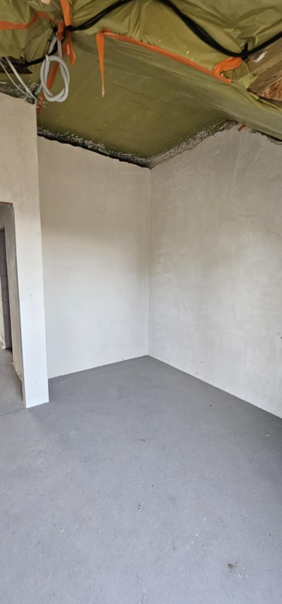 Wnętrze pokoju po szpachlowaniu ścian i wylewce podłogi, widoczne kable i izolacja na suficie.