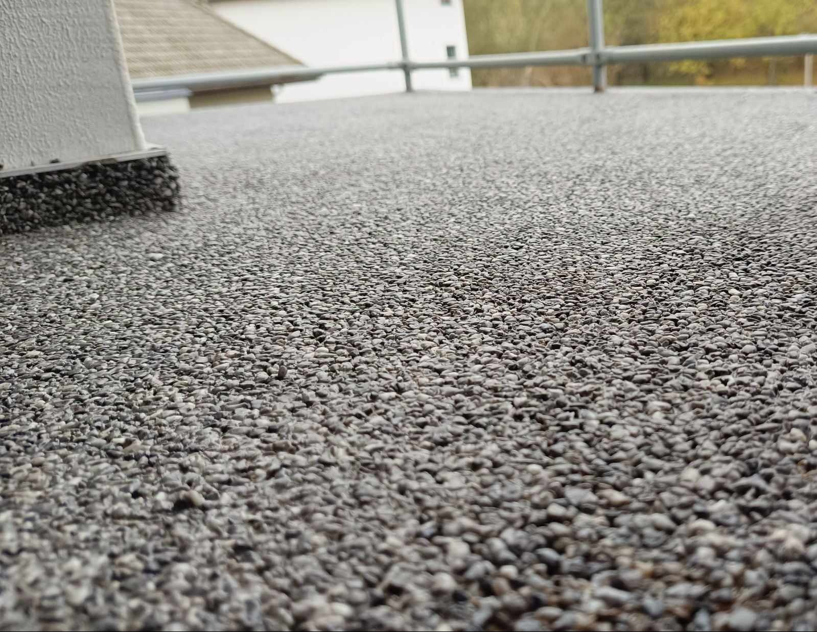 Szara posadzka żywiczna z bliska na balkonie, widoczny fragment ściany i barierki w tle.