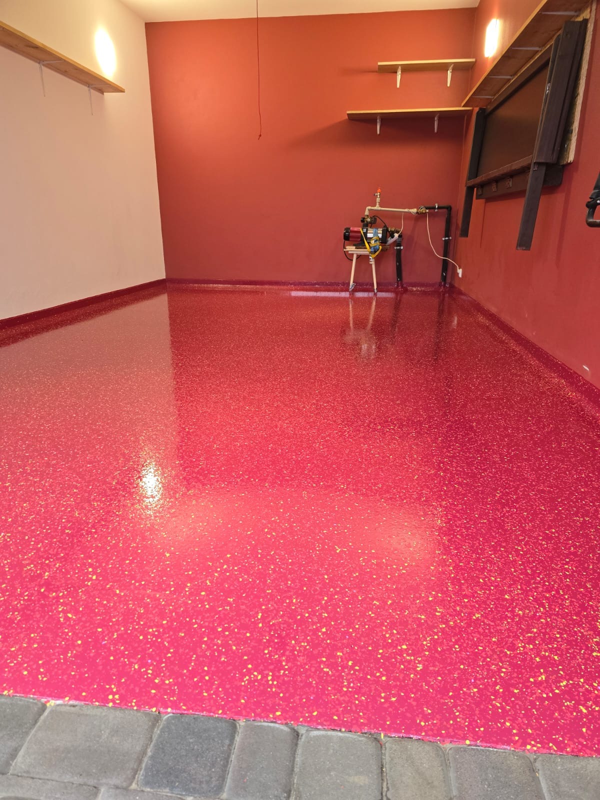 Błyszcząca, intensywnie różowa podłoga z drobnymi, złotymi plamkami, wykończona przy ścianach w kolorze bordowym, widoczna instalacja wodna na tle ściany.