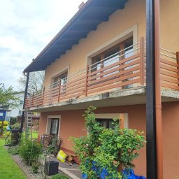 PHU GIFCIK - Dwukondygnacyjny dom z balkonami zabezpieczonymi nowoczesnymi balustradami z poziomych, drewnopodobnych listew i metalowych rurek, widok z ogrodu.