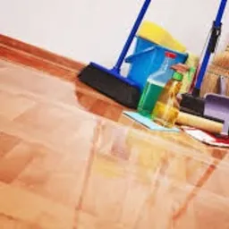 Świeżo umyta, błyszcząca podłoga parkietowa z widocznymi narzędziami do sprzątania: mop, wiadro z płynem, zmiotka i szufelka.