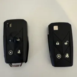 Dwa czarne kluczyki samochodowe z gumowymi przyciskami na białym tle. Jeden kluczyk jest otwarty, drugi zamknięty.