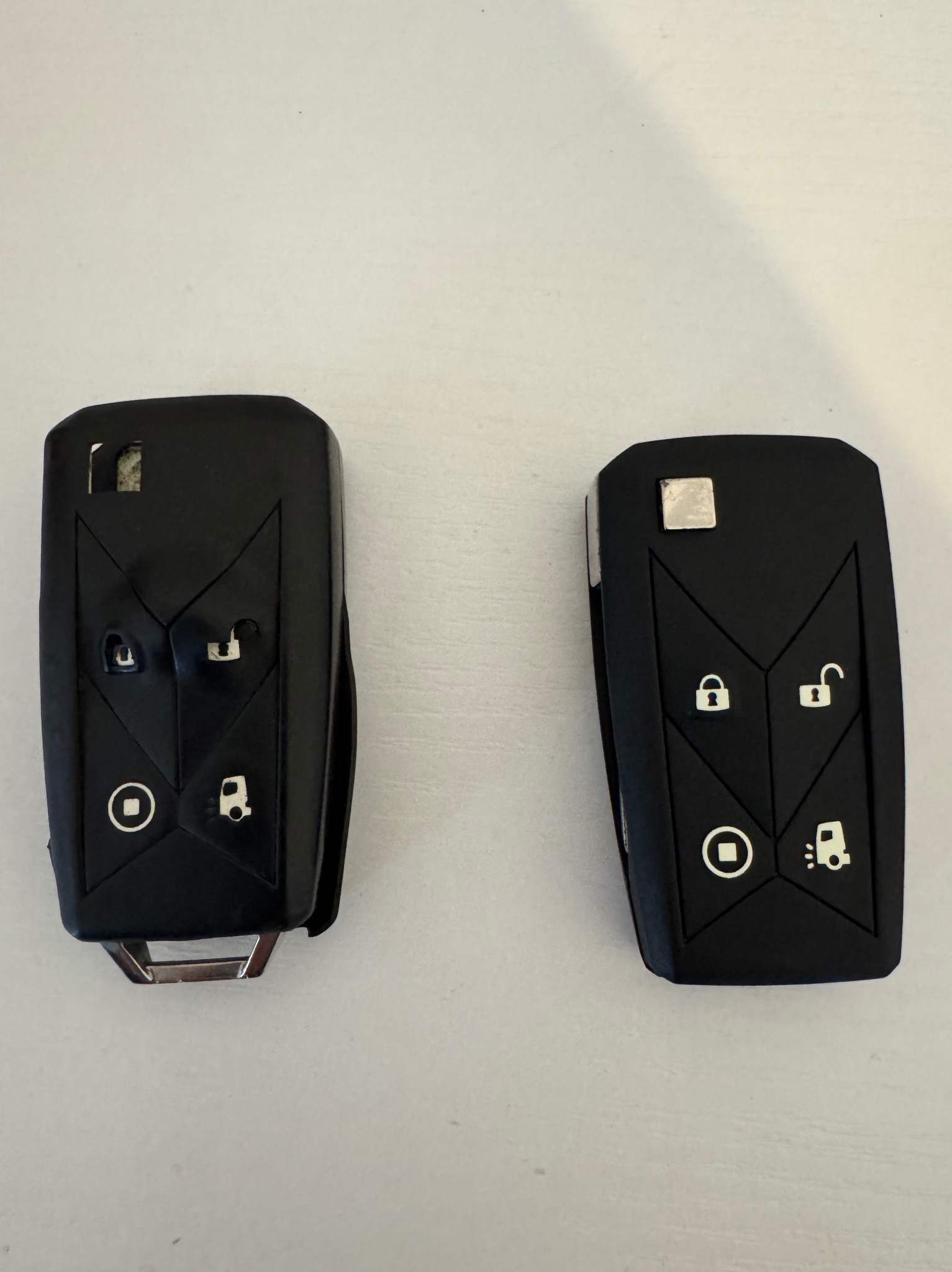 Dwa czarne kluczyki samochodowe z gumowymi przyciskami na białym tle. Jeden kluczyk jest otwarty, drugi zamknięty.
