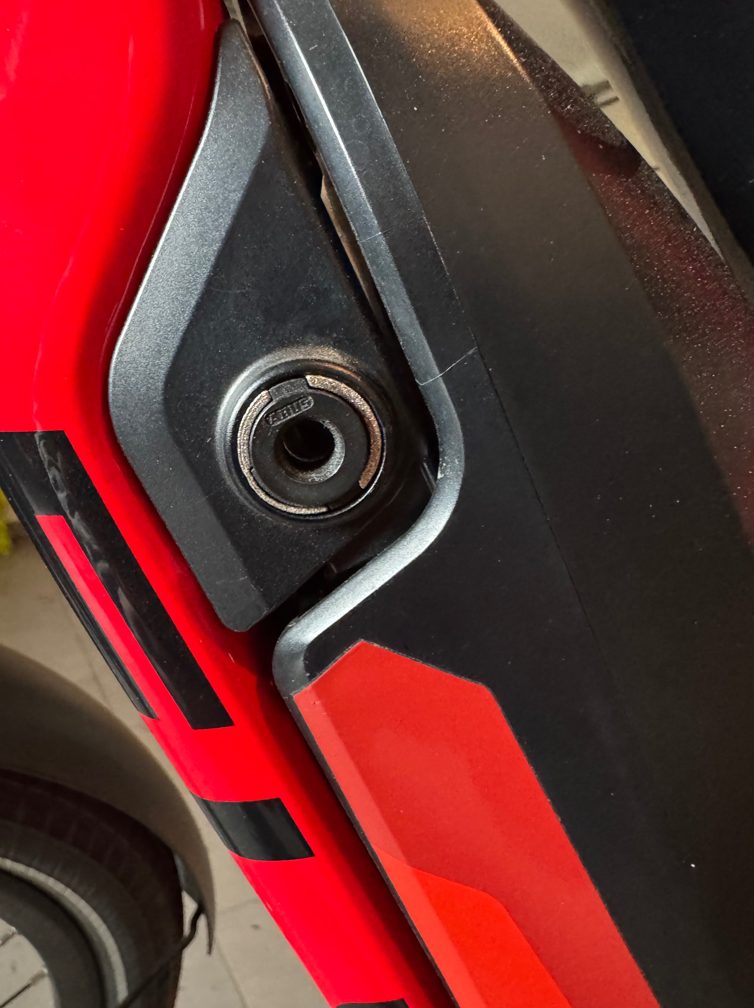 Zbliżenie na zamek ABUS w obudowie akumulatora roweru elektrycznego, czerwono-czarna kolorystyka ramy.