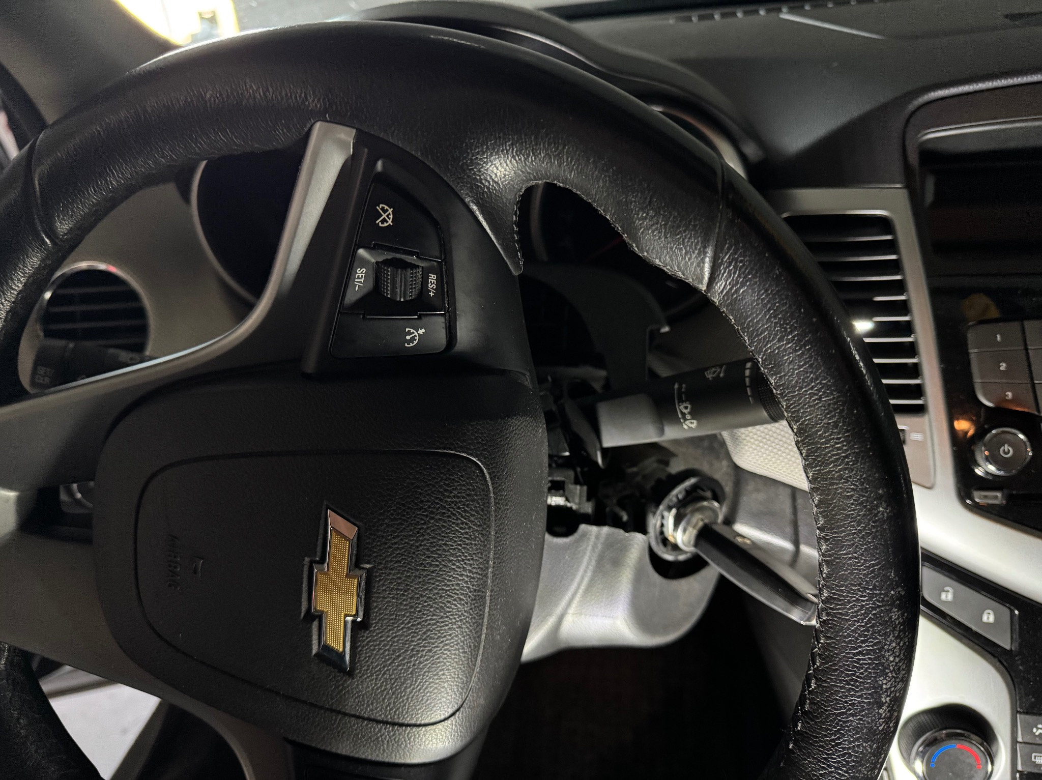 Czarna kierownica samochodu Chevrolet z widocznym uszkodzonym modułem przełączników i stacyjką z kluczykiem, wnętrze pojazdu w trakcie naprawy.