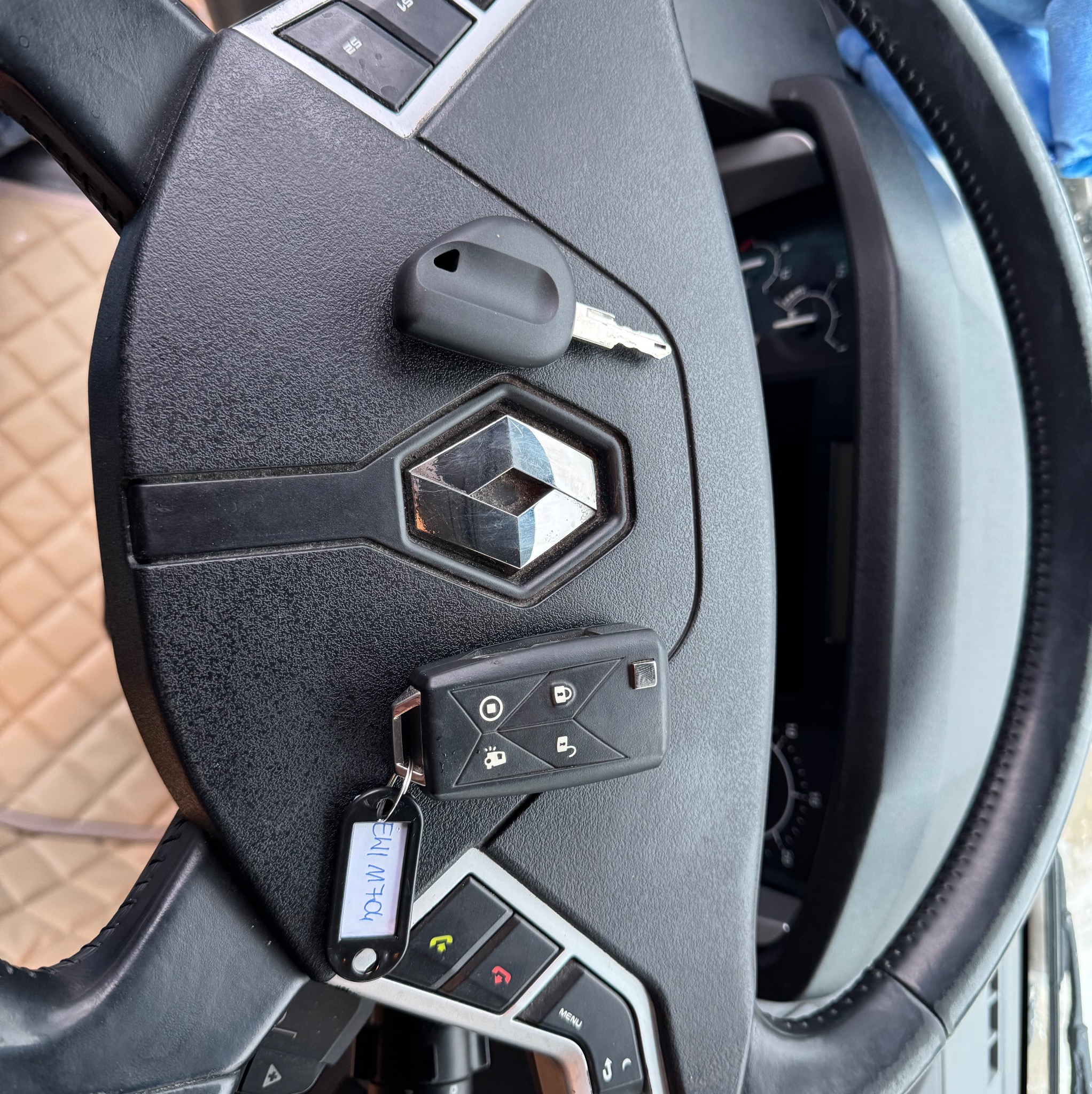 Kluczyki do Renault leżące na kierownicy, widoczne logo Renault oraz przyciski funkcyjne na kierownicy.